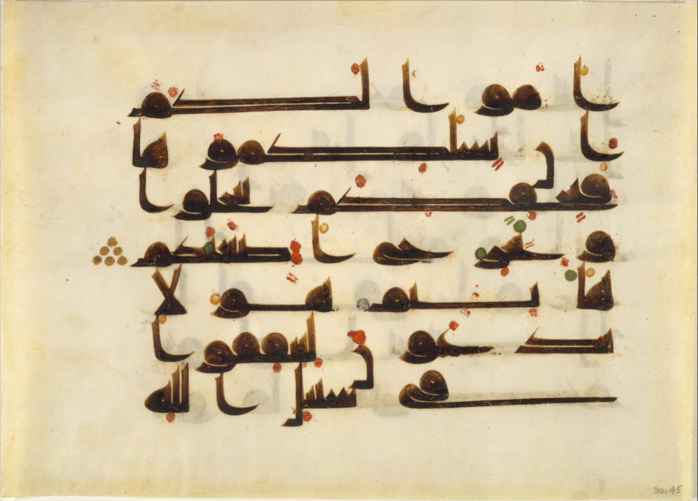 A parchment page of Kufic Arabic script. The consonants are written large in brown ink; small red and green dots are scattered around and between them, marking vowels the letters themselves do not carry.